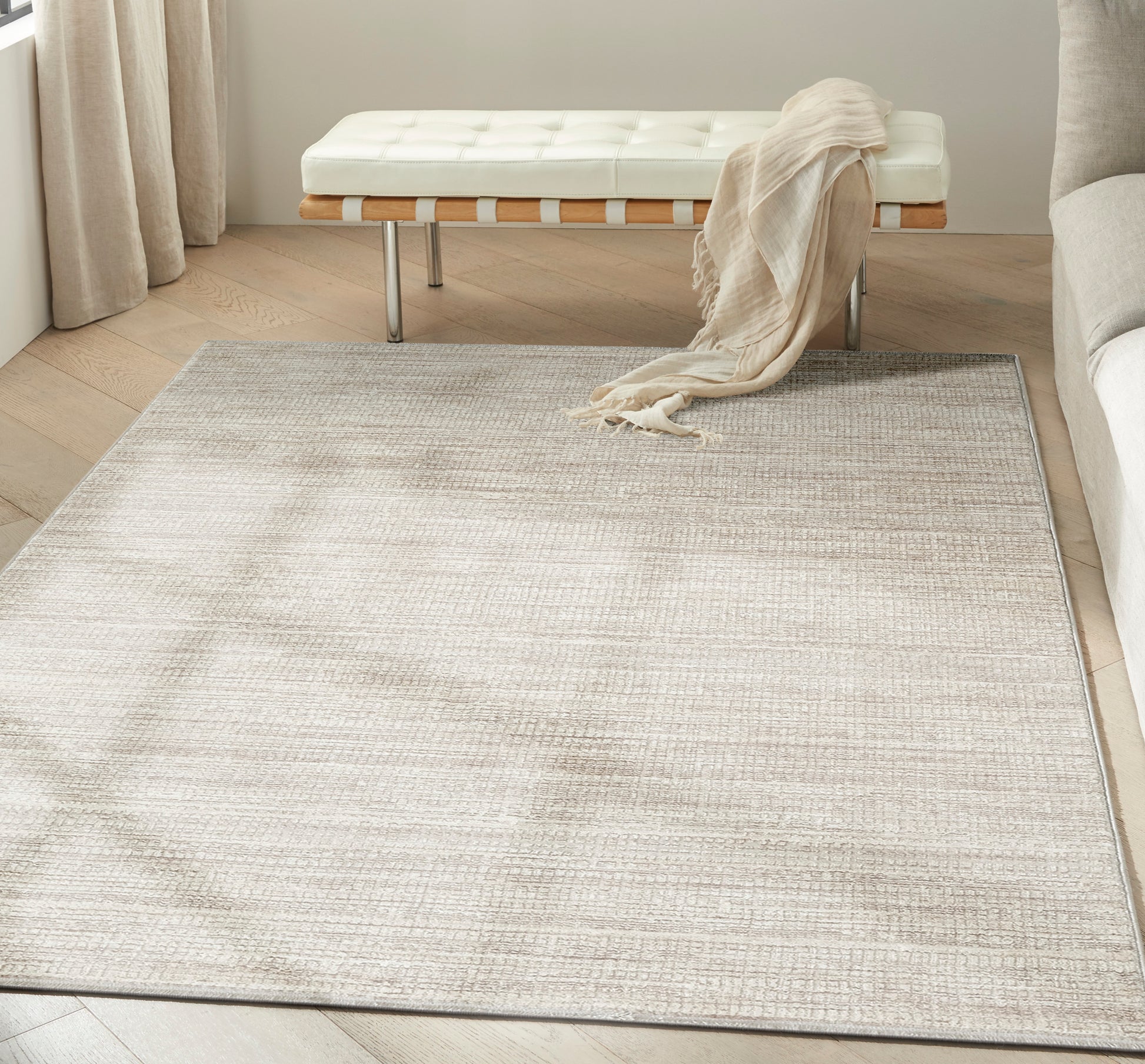 Neutral beige woven area rug in a light living room with a white tufted bench, beige throw, and light wood floors.