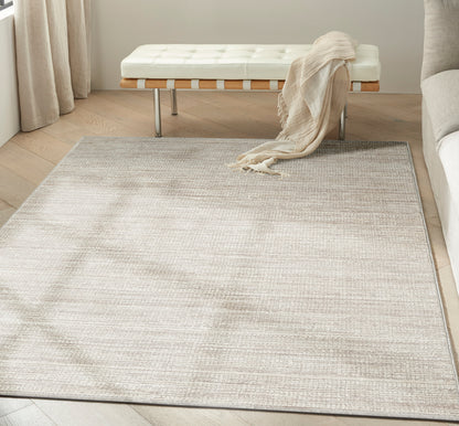 Neutral beige woven area rug in a light living room with a white tufted bench, beige throw, and light wood floors.