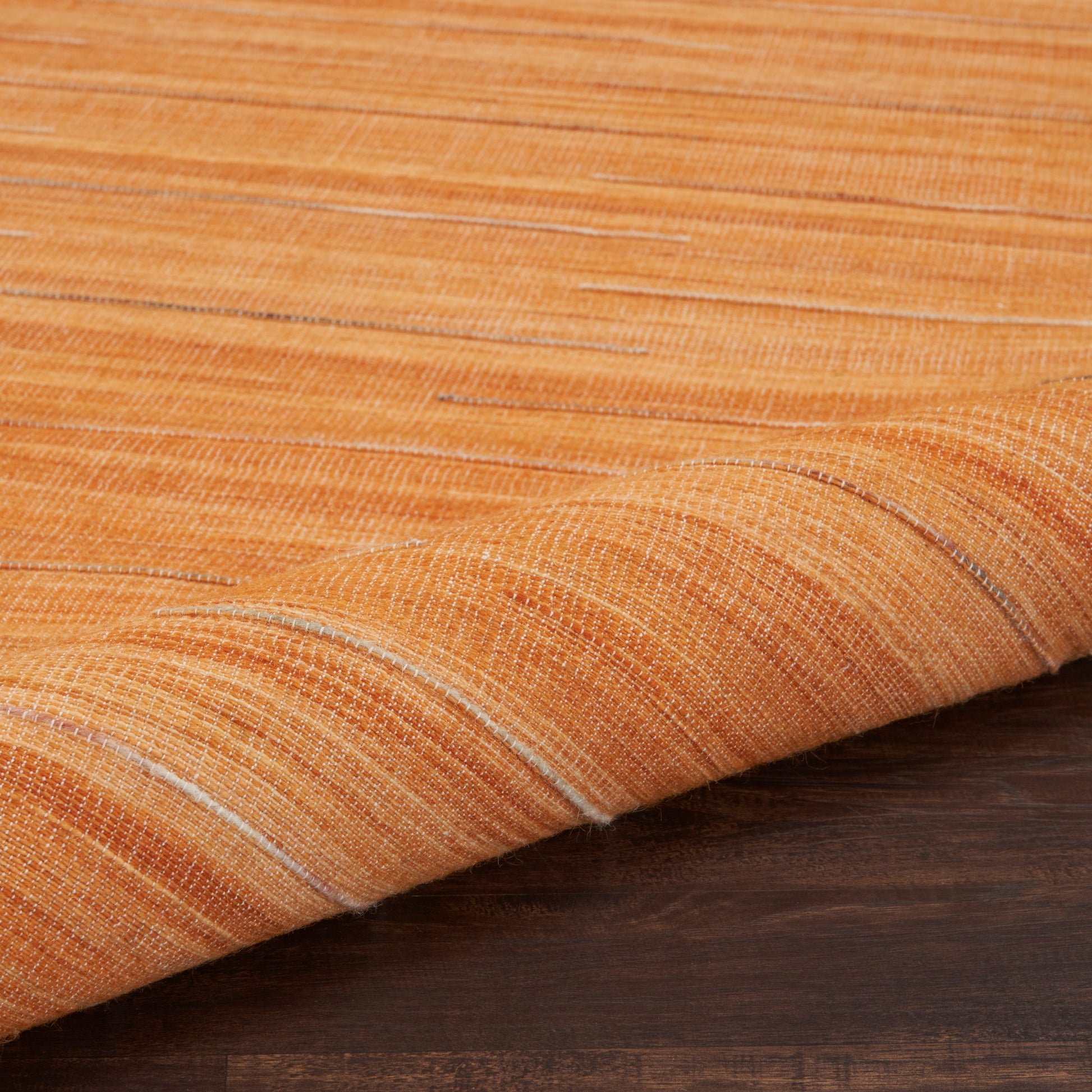 Orange woven rug with subtle light stripes, draped over a dark wood surface.