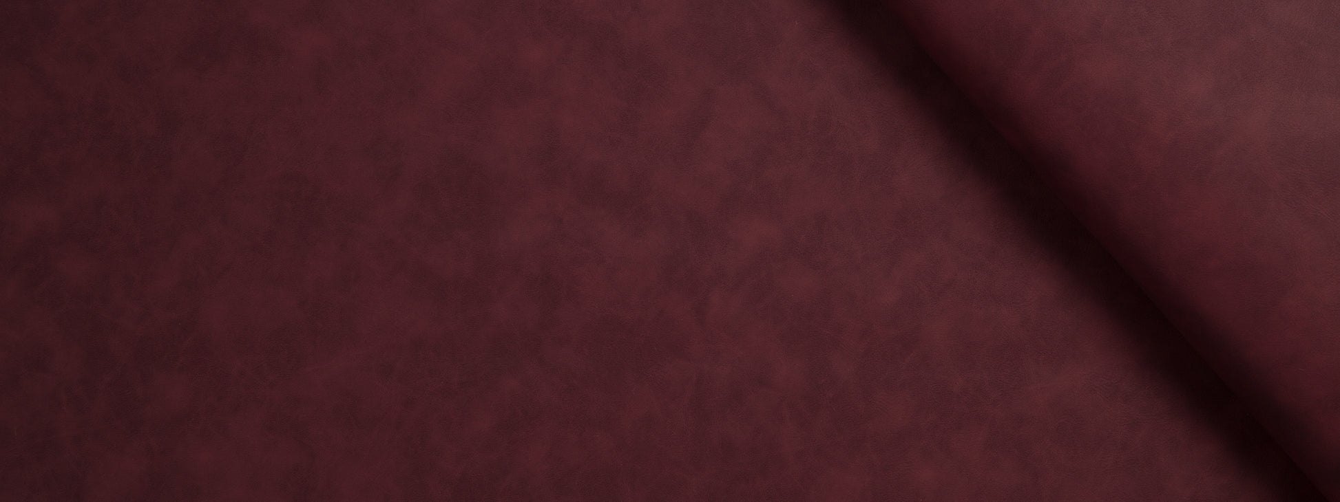 Close-up of burgundy velvet fabric with soft nap and a diagonal fold.