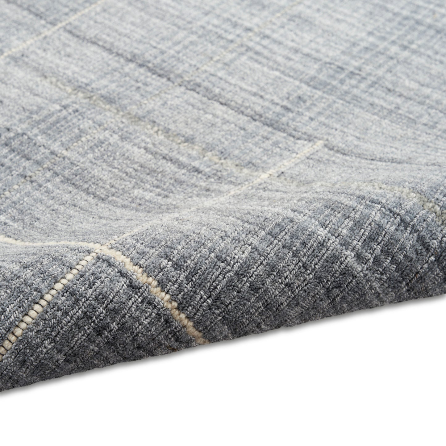 Blue-gray geometric rug with subtle light lines, rich woven texture, folded corner exposing stitched edge.