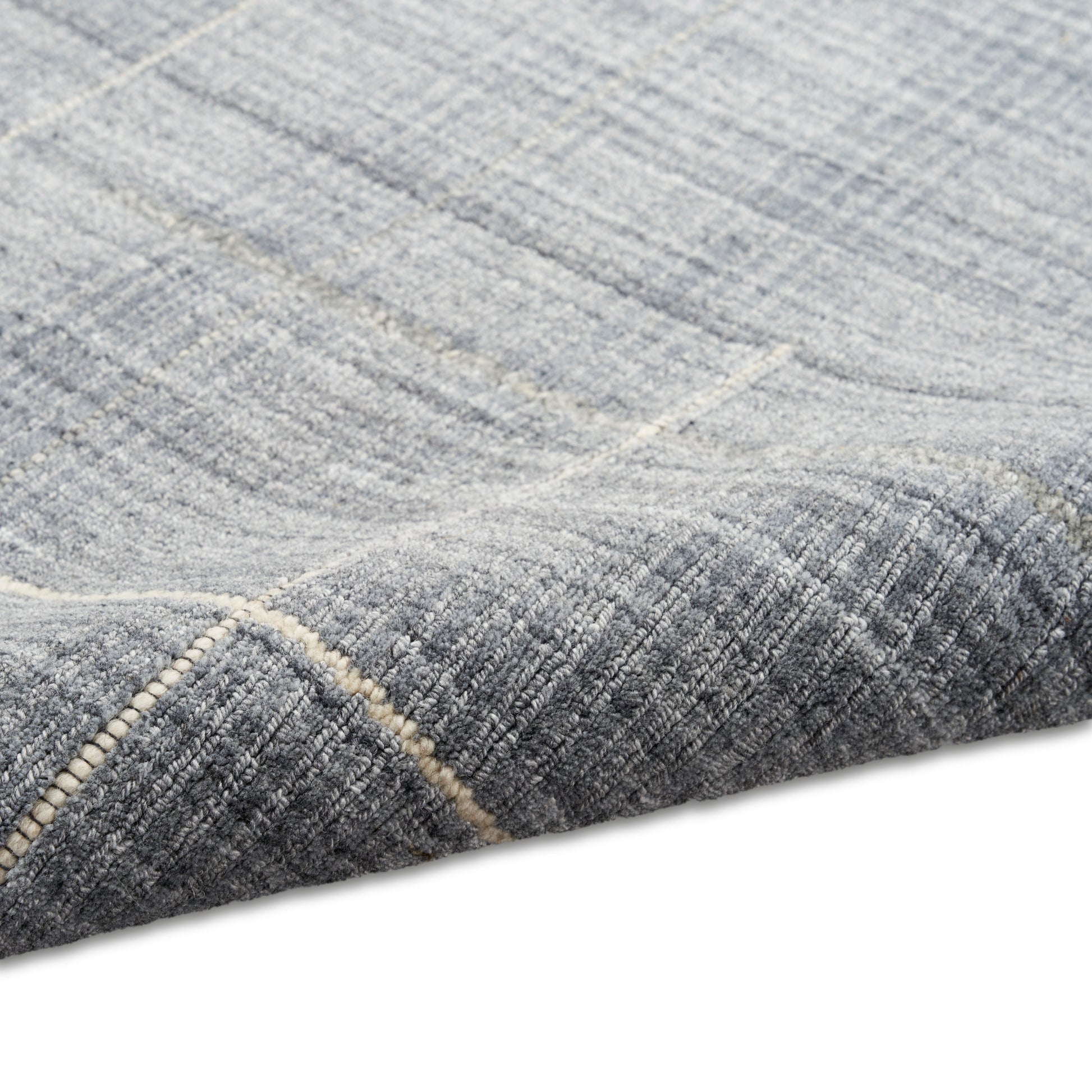 Blue-gray geometric rug with subtle light lines, rich woven texture, folded corner exposing stitched edge.