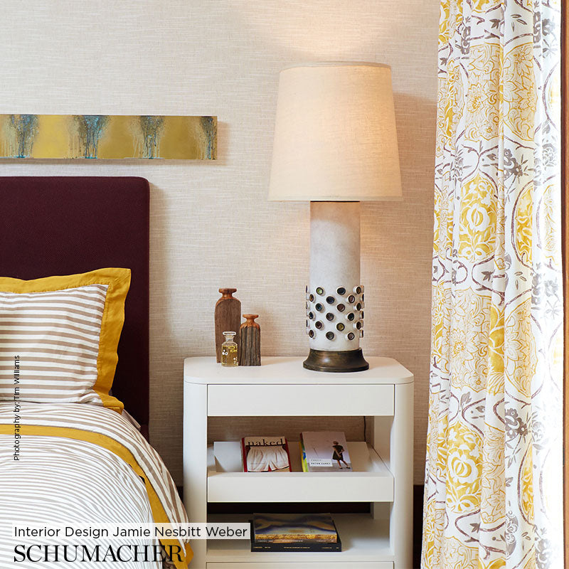 White nightstand with drawer and shelf, ceramic perforated-base lamp, burgundy headboard bed, yellow accents, curtains.