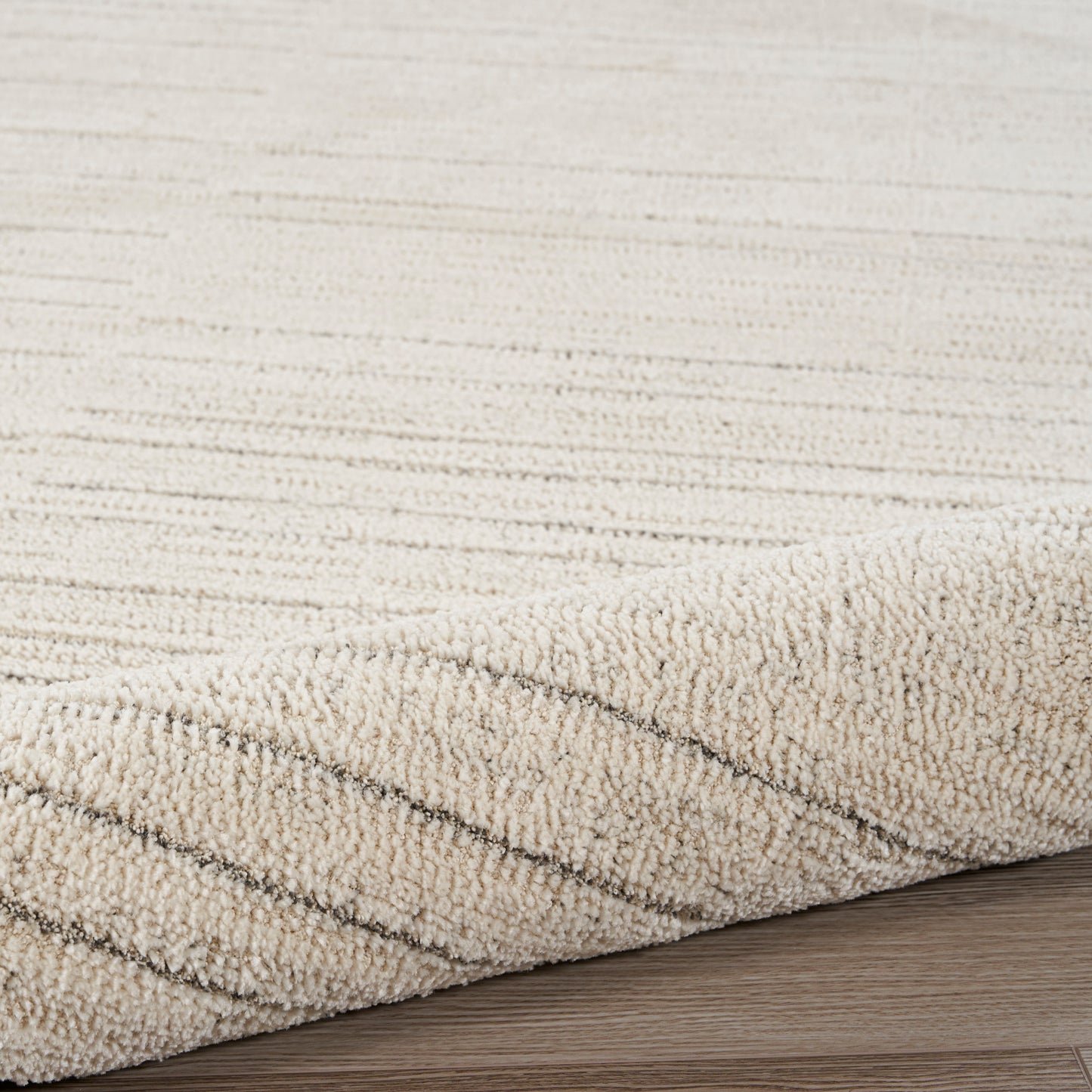 Beige textured rug with loop pile and subtle diagonal stripes along edge on wood floor.