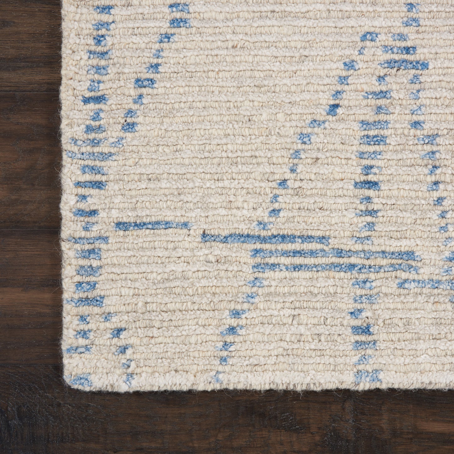 Cream shag rug with pale blue geometric lines on dark wood floor; contemporary wool texture.