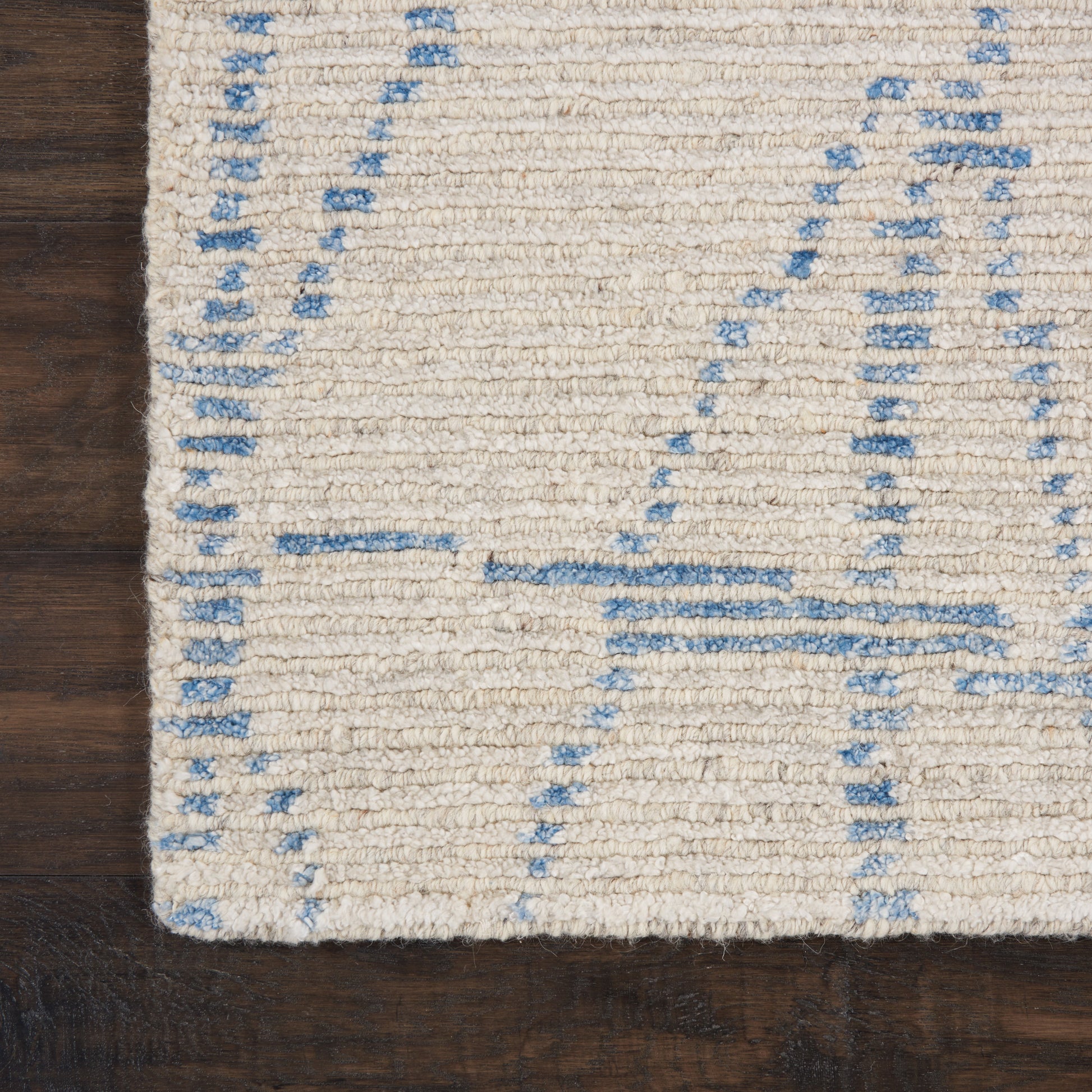 Cream shag rug with pale blue geometric lines on dark wood floor; contemporary wool texture.
