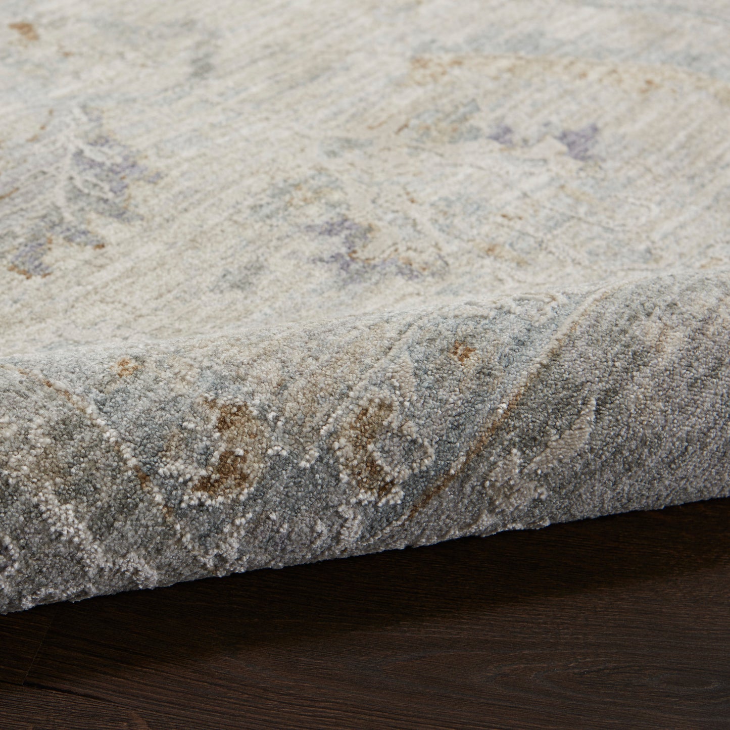 Soft gray and ivory distressed rug with subtle floral motif and plush pile on dark wood floor.