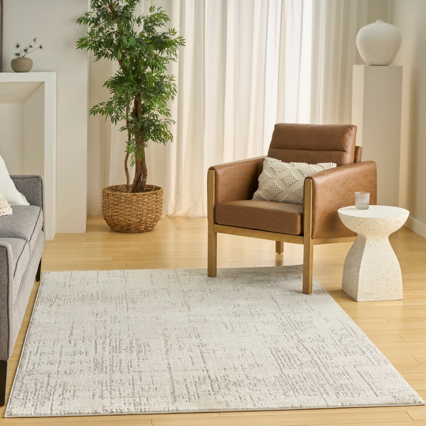 Brown leather armchair with wooden legs in a bright living room, beige rug, gray sofa, and potted plant.