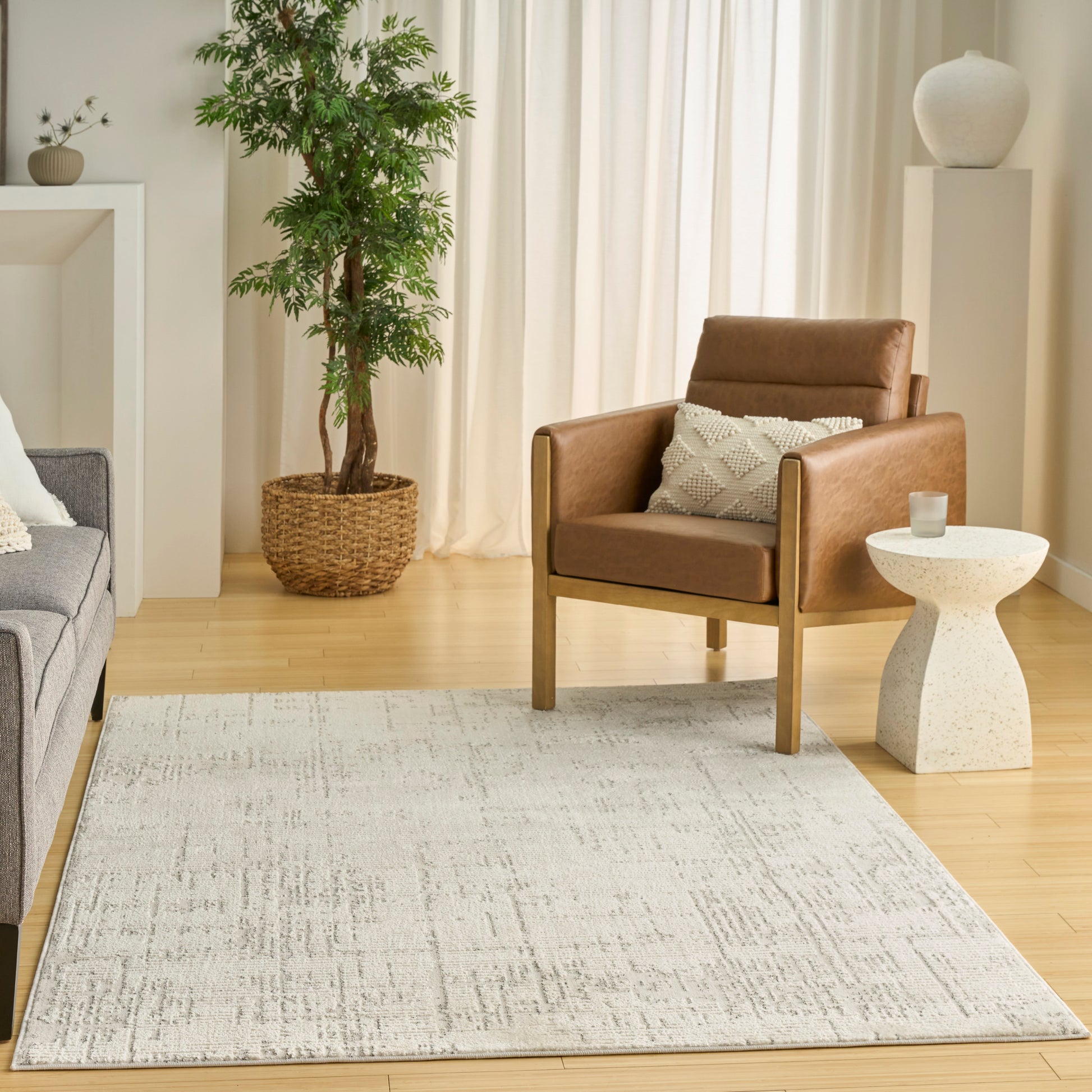Brown leather armchair with wooden legs in a bright living room, beige rug, gray sofa, and potted plant.