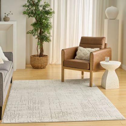 Brown leather armchair with wooden legs in a bright living room, beige rug, gray sofa, and potted plant.
