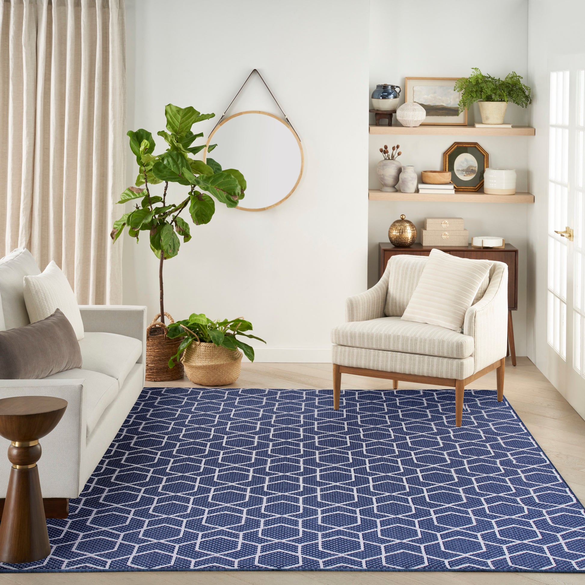 Navy blue geometric lattice rug in a bright neutral living room with cream sofa, striped armchair and potted plants.