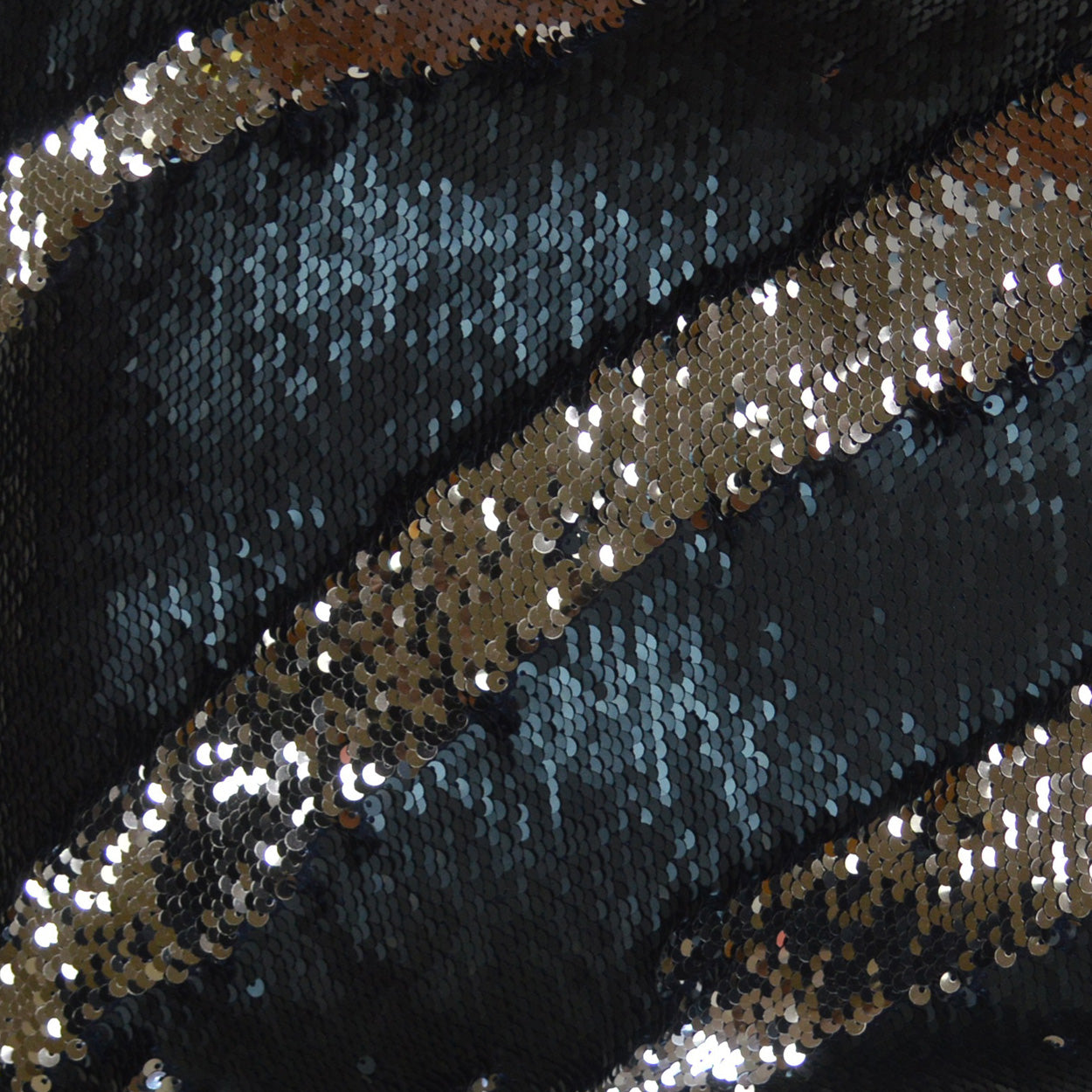 Diagonal bands of gold and navy sequins on dark fabric; glittery, festive textile.
