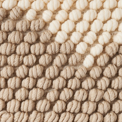 Close-up of chunky beige boucle yarn with thick knotted loops; warm textured rug.