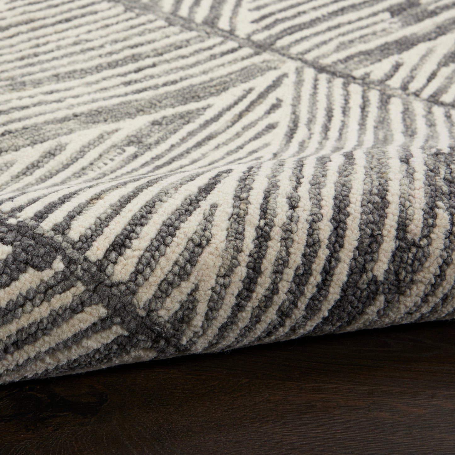 Close-up of a gray and off-white striped area rug with a textured loop-pile on a dark wood floor.