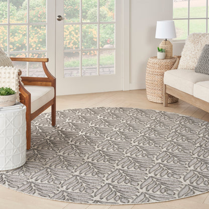 Round gray rug with leaf motif in sunlit living room; wood chair, wicker side table, beige sofa, French doors.