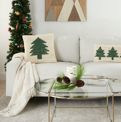Cozy living room with Christmas tree, beige sofa, knitted green-tree cushions, throw, glass coffee table with pinecones.