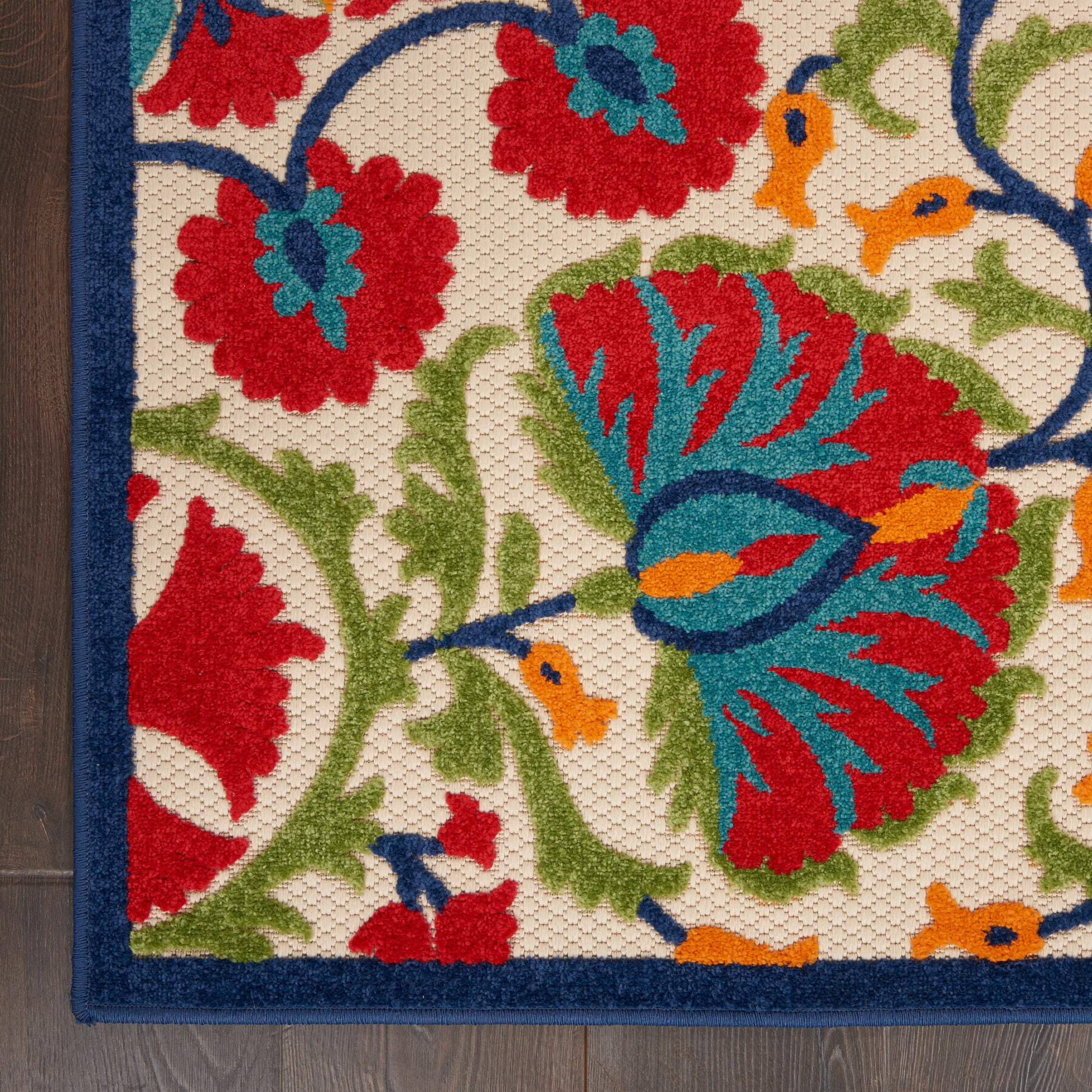 Rectangular woven rug with cream background and vibrant red, blue, green floral pattern; navy border and textured pile.