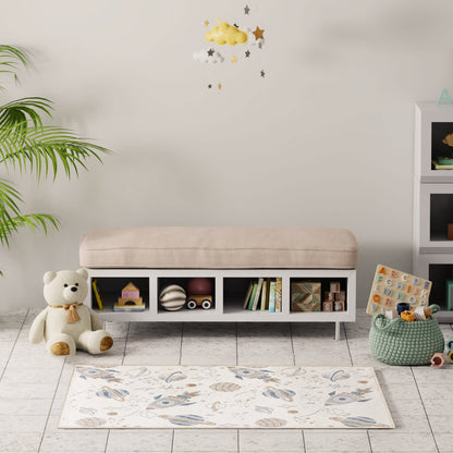 White low storage bench with beige cushion and open cubbies holding toys and books; cozy kids' room with plant and rug.