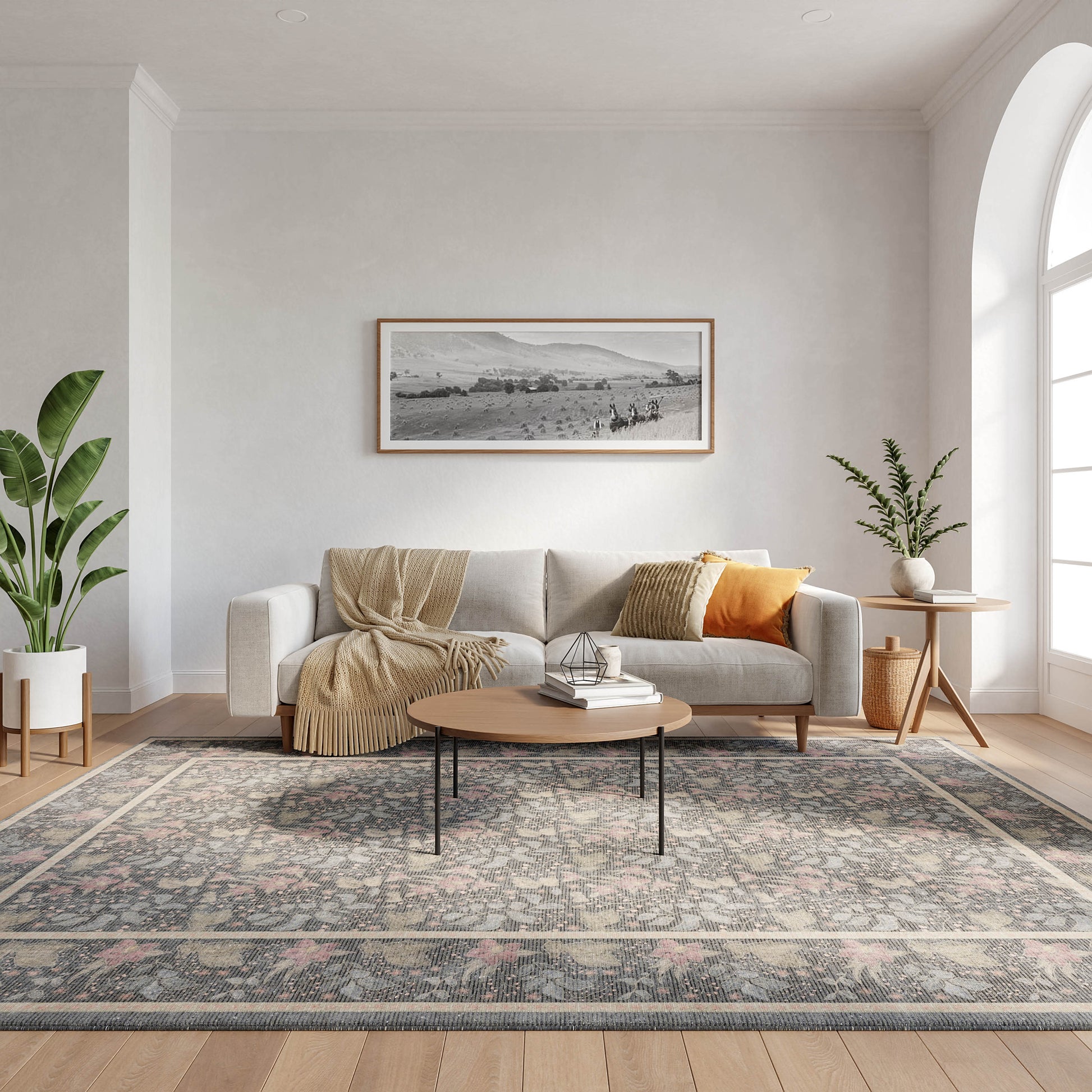 Modern living room with gray sofa, beige throw, orange cushion, coffee table, patterned rug, plants, arched window, art.