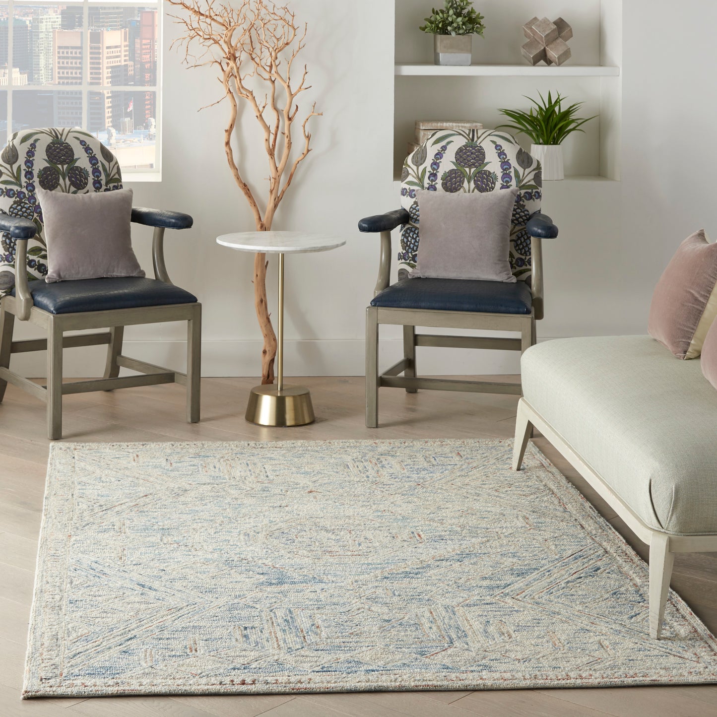 Bright living room with a light blue patterned rug, two navy armchairs with floral cushions, and a round white side table.