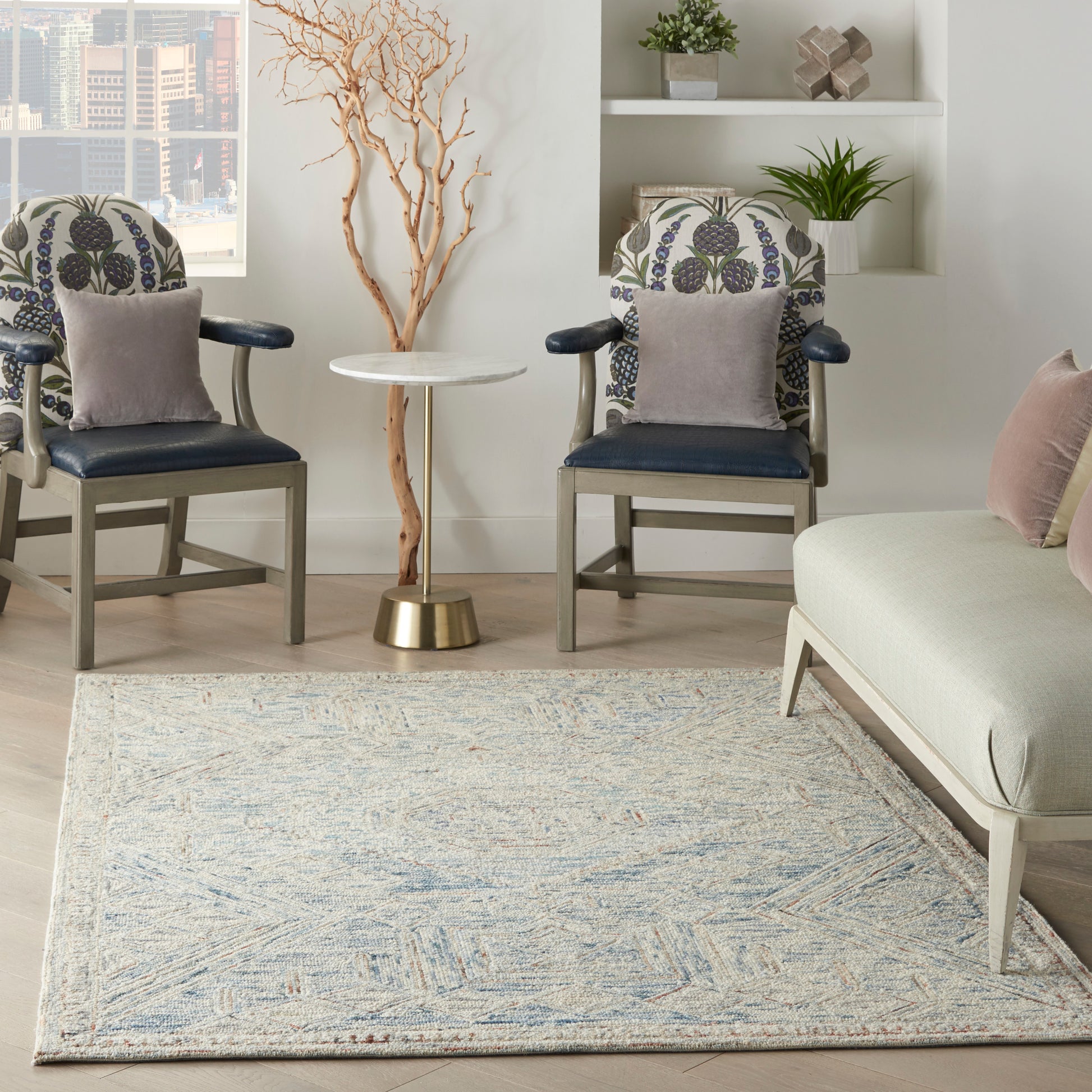 Bright living room with a light blue patterned rug, two navy armchairs with floral cushions, and a round white side table.