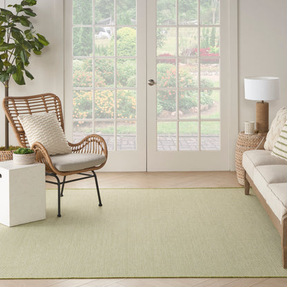 Bright living room with a woven rattan chair, beige sofa, light green area rug, potted plant, and glass French doors.