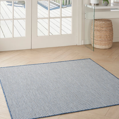 Light blue flat-weave rug with a tiny geometric pattern and a dark blue border; 5' x 5' square rug on light wood floor.
