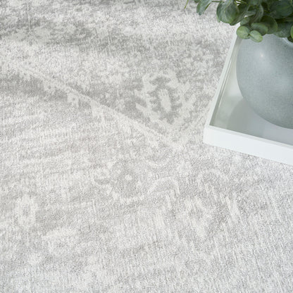 Light gray patterned round rug with a white tray holding a round gray planter and a green leafy plant