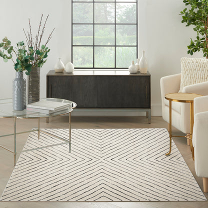 Modern living room with a beige chevron rug, glass coffee table, dark wood sideboard, cream seating and green plants.