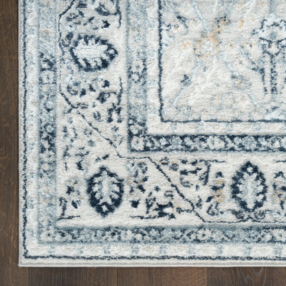 Light gray-blue oriental-style area rug with floral border on dark wood floor.