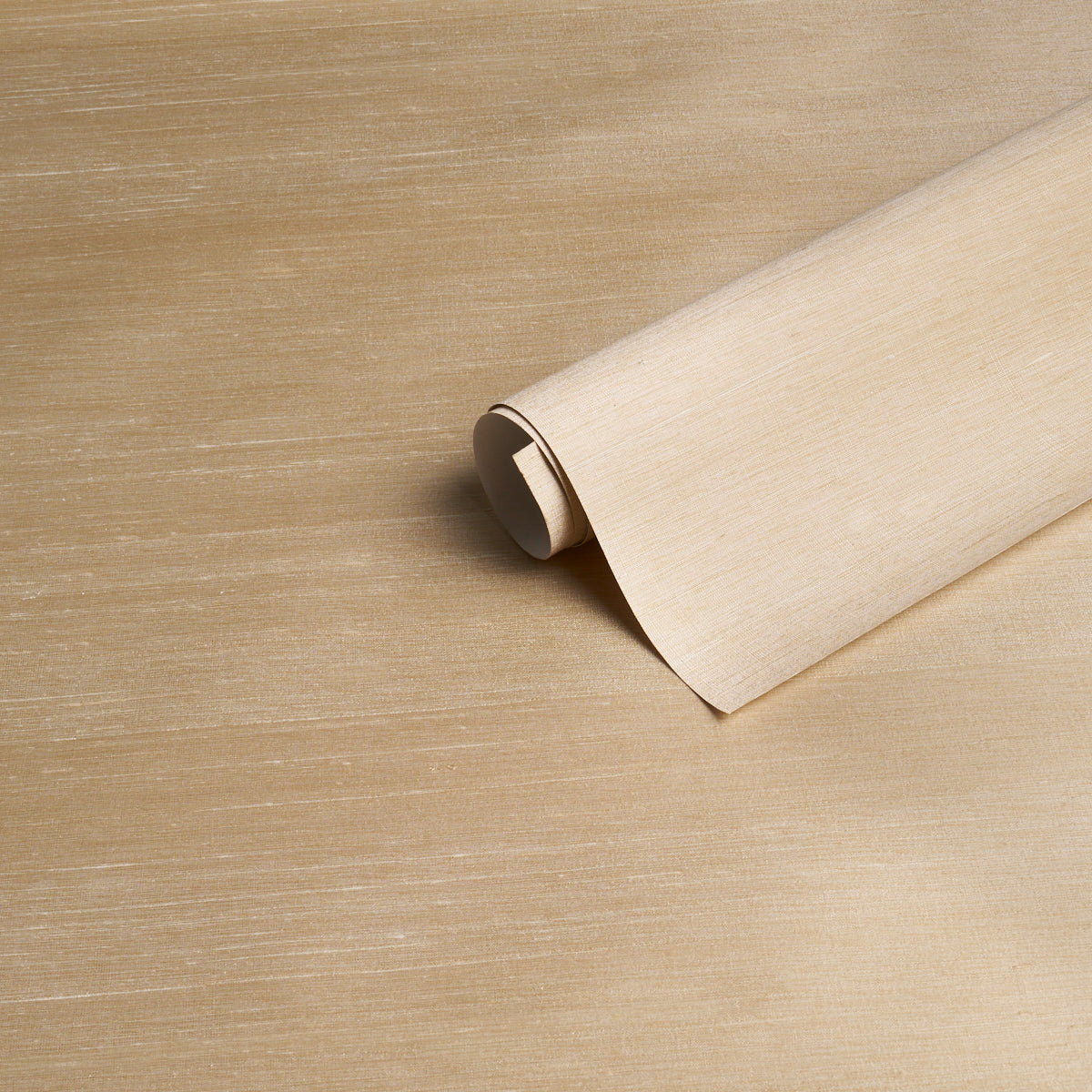 Beige wallpaper roll partially unrolled on a tan wooden surface, showing a parchment-like textured pattern.