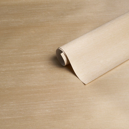 Beige wallpaper roll partially unrolled on a tan wooden surface, showing a parchment-like textured pattern.