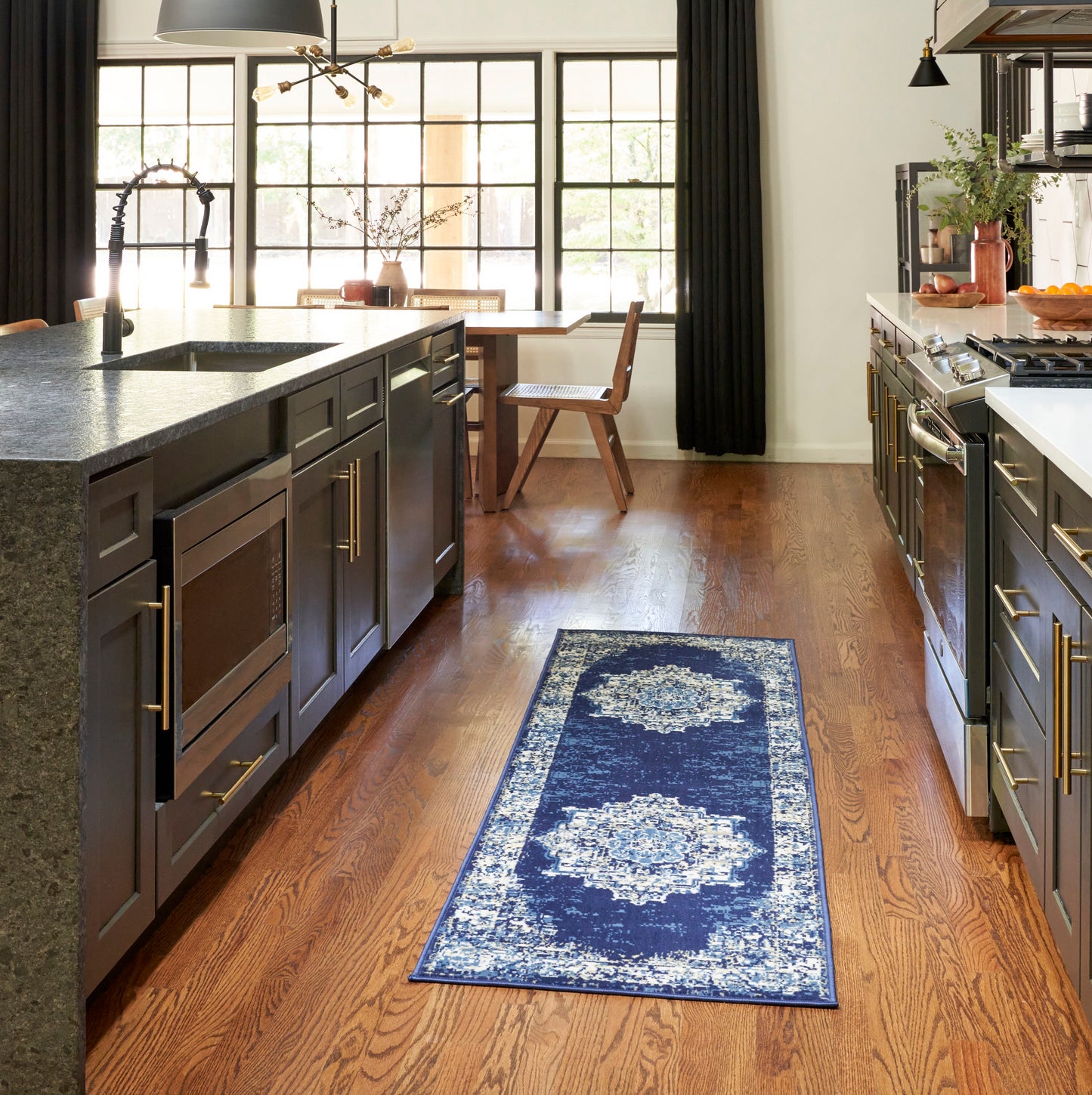 Navy blue patterned rug runner in a modern kitchen with dark cabinetry, stone island, and wood floors.