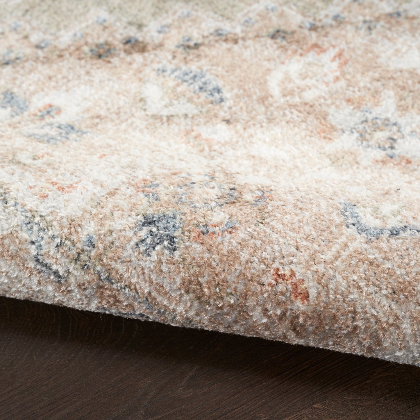 Soft plush beige area rug with blue, cream and peach accents in an abstract floral pattern.