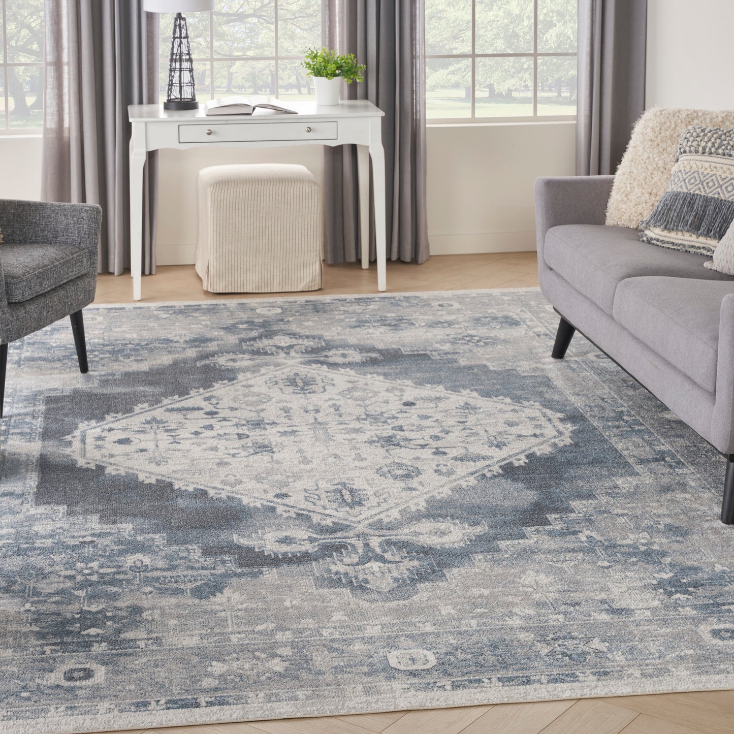 Blue-gray distressed oriental rug anchors a bright living room & gray sofa, white console & beige ottoman.