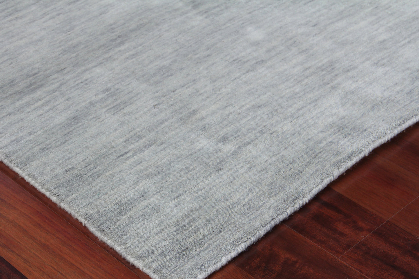 Soft light-gray rectangular area rug with subtle texture and short fringe on dark wood floor.