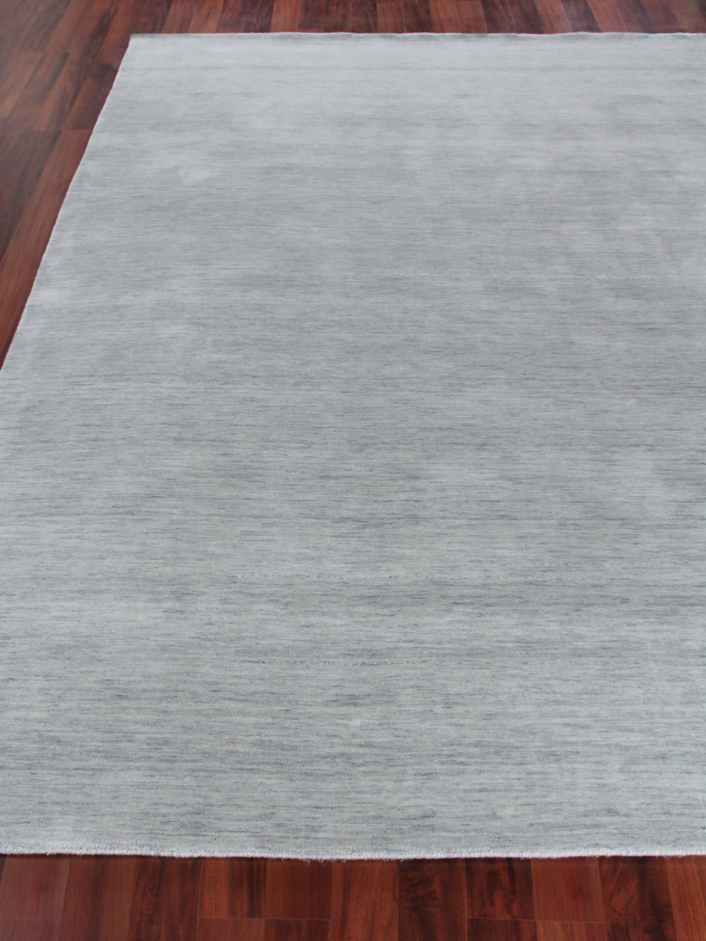 Light gray rectangular area rug with subtle texture on dark hardwood floor.