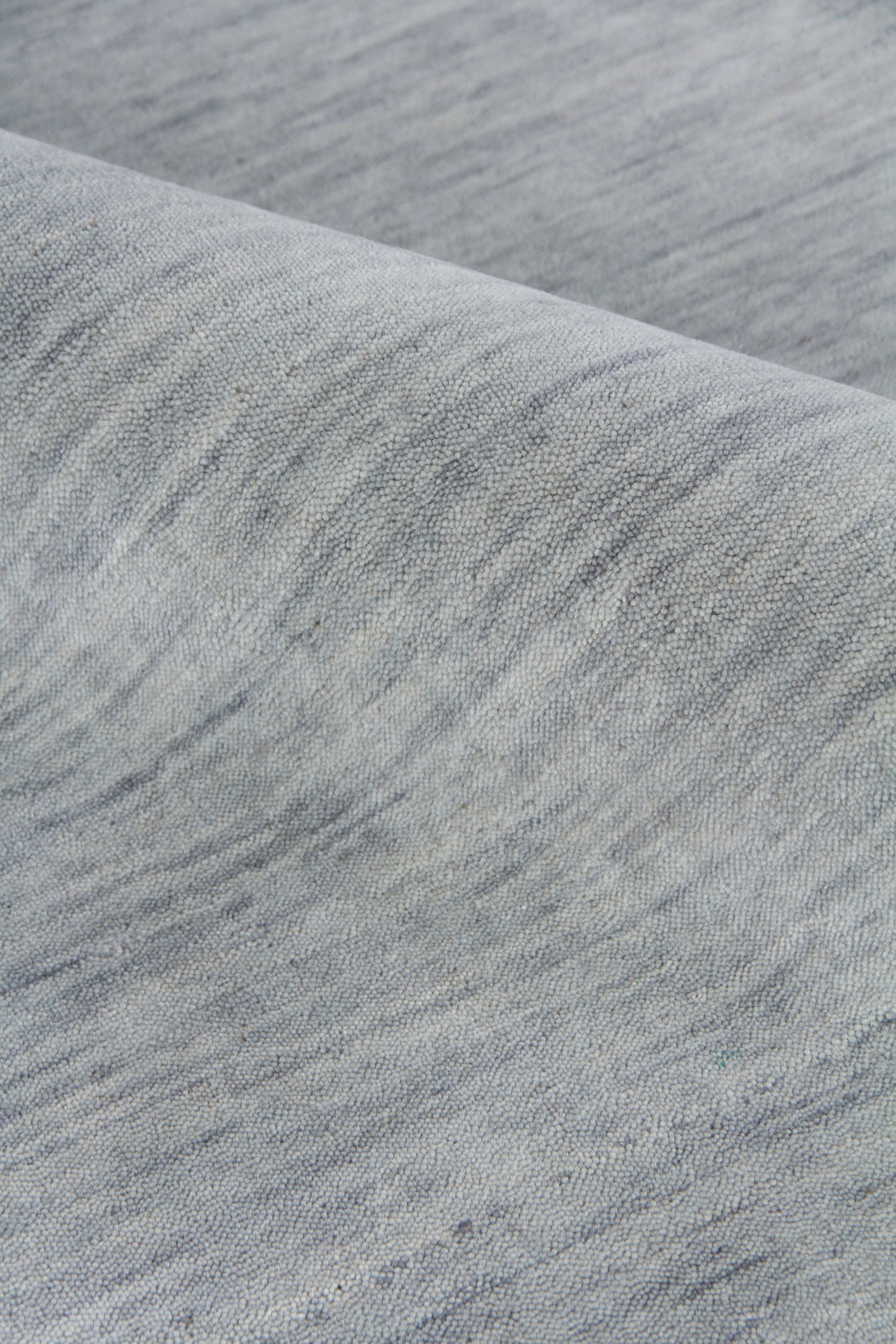 Close-up of light grey heathered rug with a soft brushed texture and a curved folded edge.