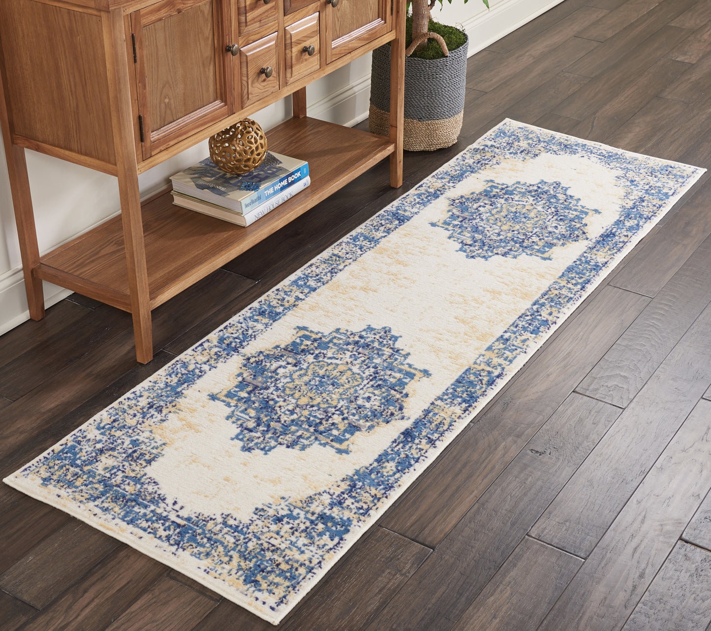Long beige runner rug with blue medallion motifs and border on dark hardwood beside a wooden console.