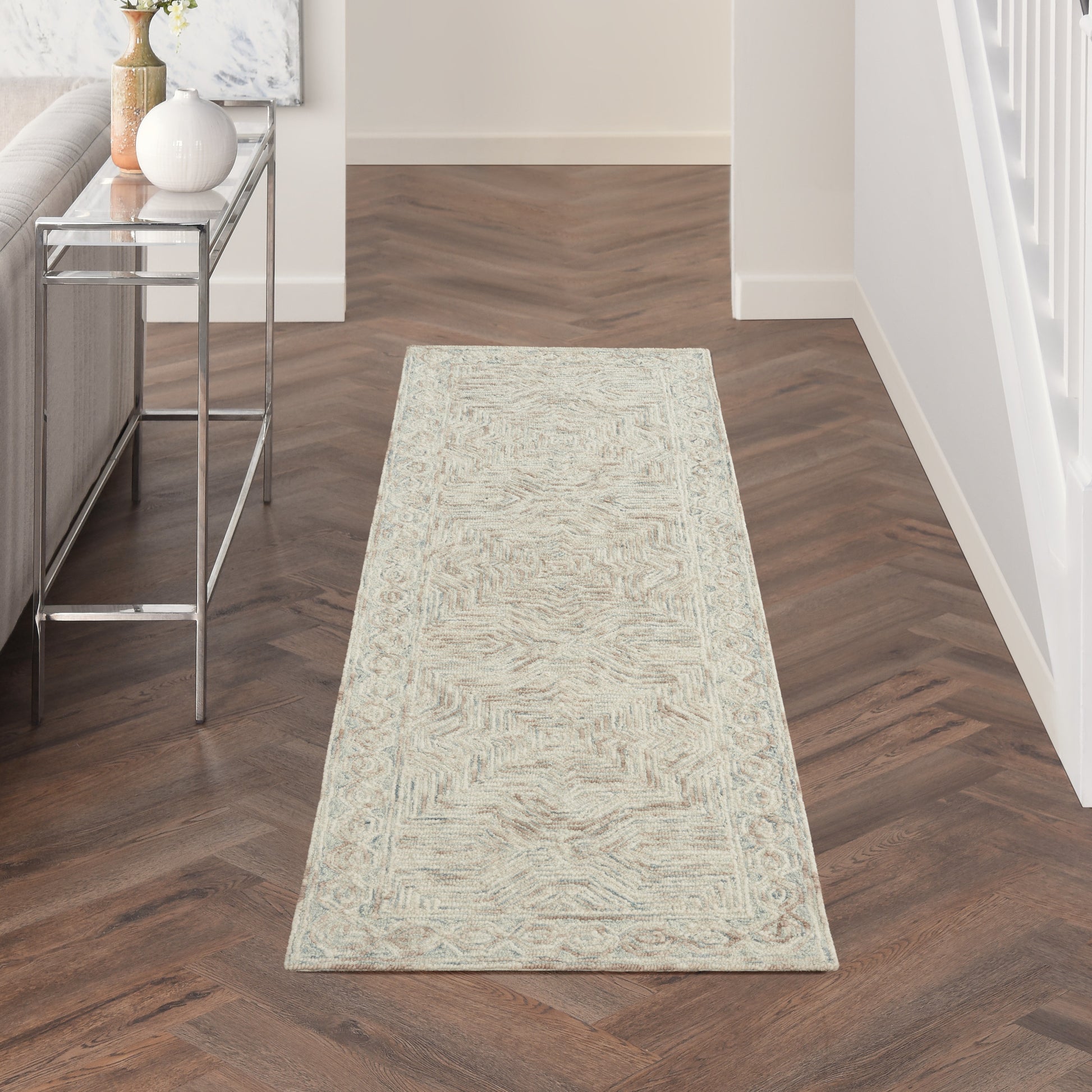 Light beige patterned hallway runner rug on dark wood floor, with a chrome-glass console table to the left.