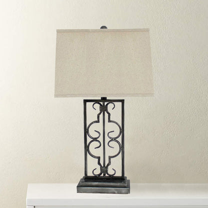 Ornate black metal scrollwork table lamp with a beige fabric shade on a white surface.
