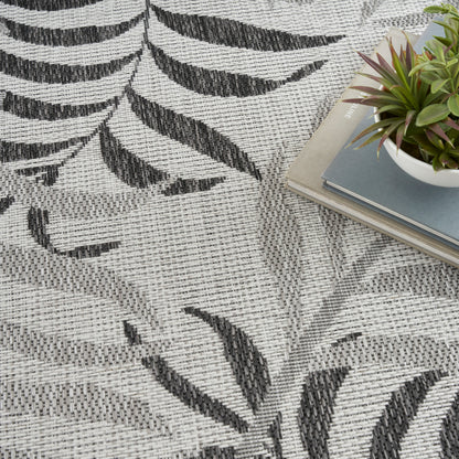Close-up of gray woven rug with black leaf pattern; a stack of books with a small potted succulent on top.