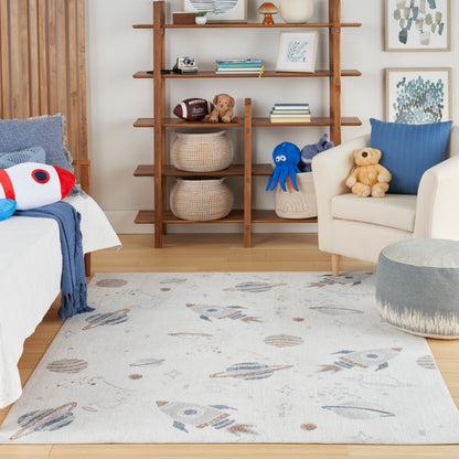 Light kid's rug with rockets and planets in blue/beige tones, in a cozy room with wooden bookshelf and stuffed toys.