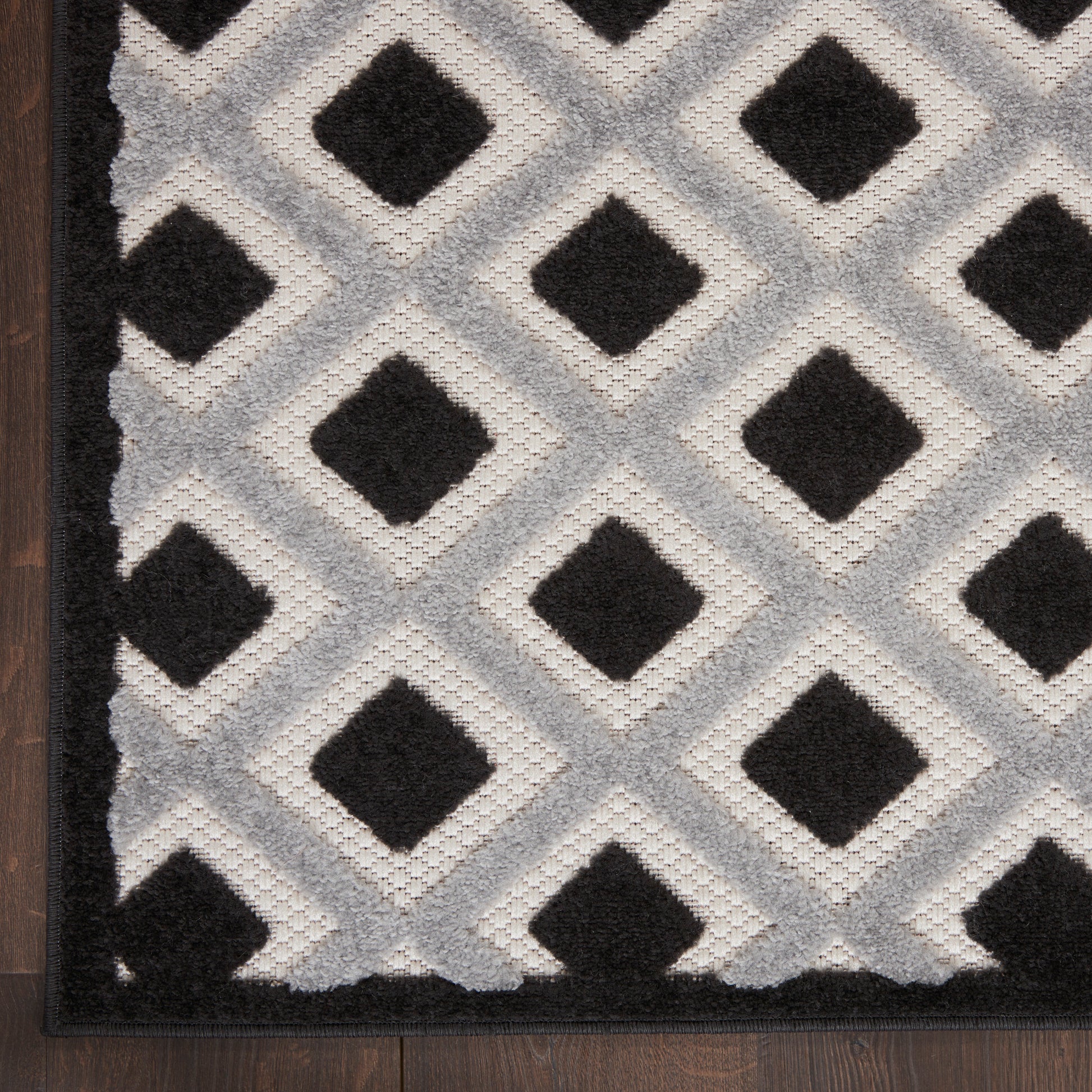 Large neutral gray 9' x 12' rug on wood floor with a dark patterned design; minimalist decor piece.