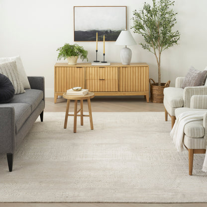 Mid-century living room: light wood sideboard, gray sofa, beige armchairs, round coffee table, potted plant, candles, lamp.
