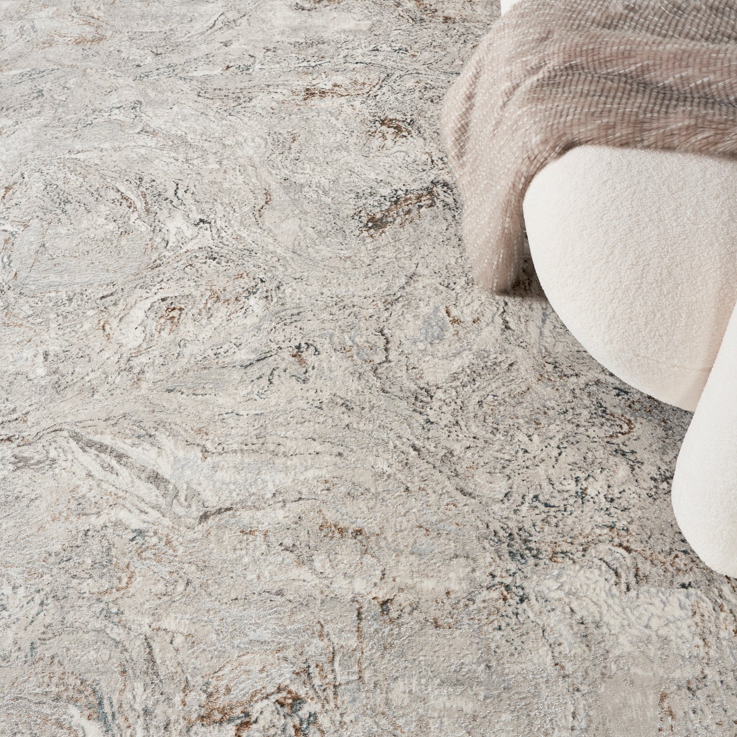 Cream beige textured rug with abstract marbled pattern and a plush beige throw draped over a curved armchair.