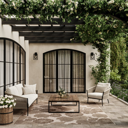 Beige tropical rug 6' x 9' on a patio under outdoor seating; cream cushions, wicker chairs, wooden coffee table, and lush greenery.