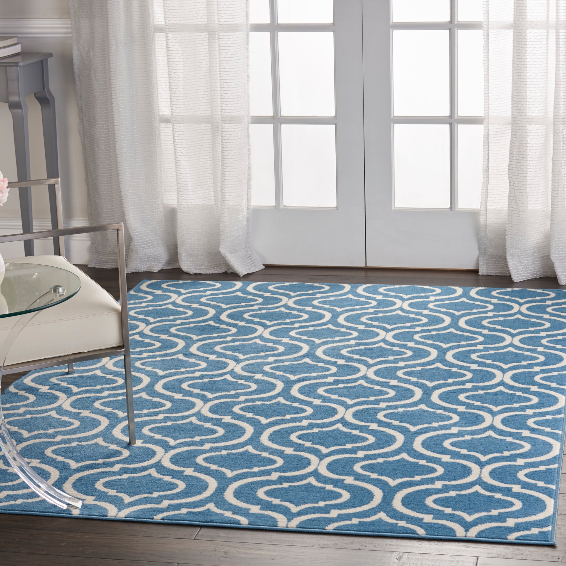 Blue rug with white wavy pattern in a bright living room by glass doors; modern glass coffee table nearby.