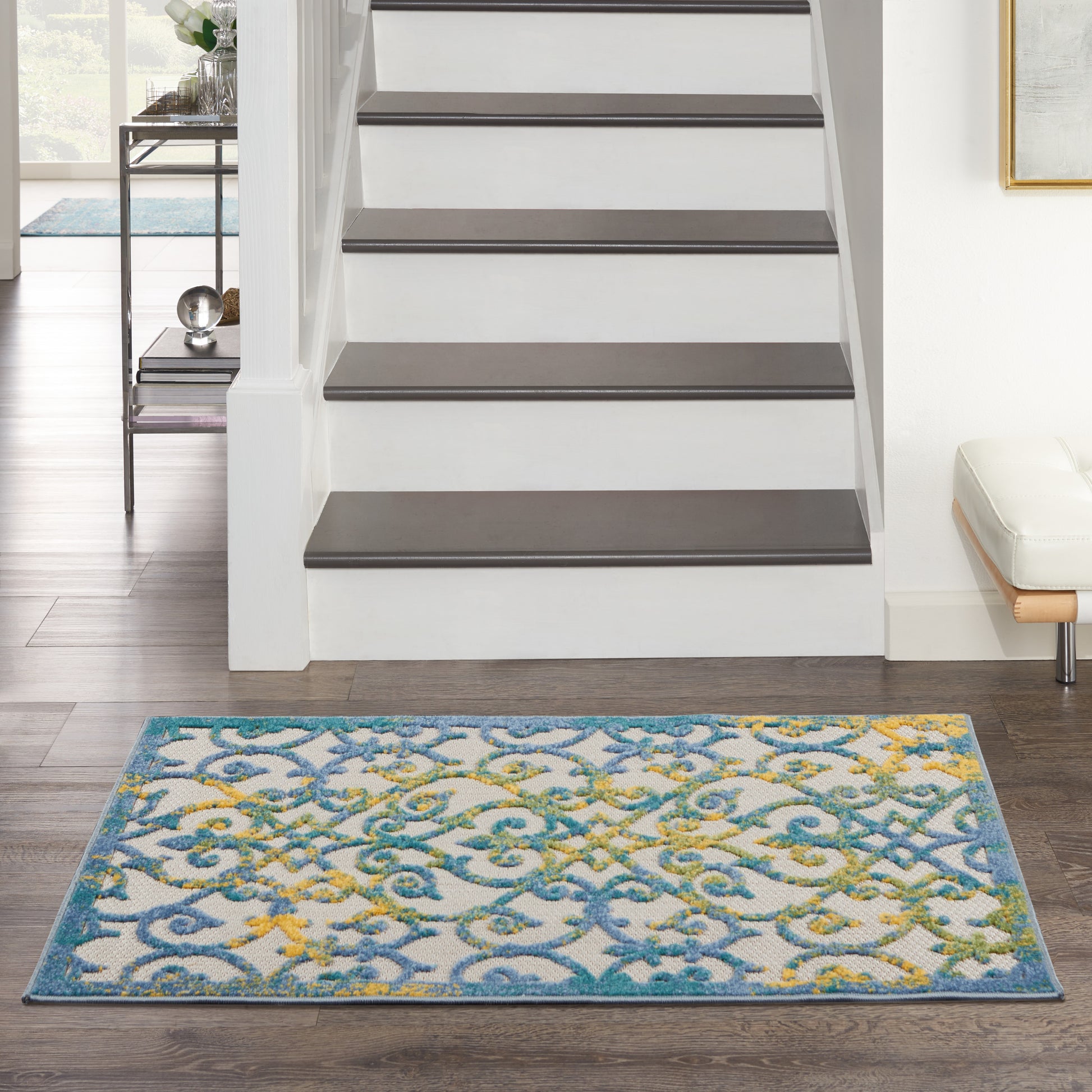 Colorful blue, teal and yellow patterned rug in front of white staircase with dark treads; modern living room.
