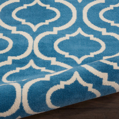 Blue rug with white geometric lattice pattern, folded corner on dark wood floor.